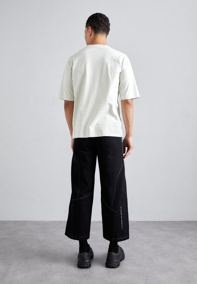 Lys grå t-shirt med korte ærmer, parret med sorte bukser med brede ben, der har hvide stiksøm og kraftige sorte sneakers.