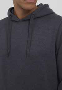 Sweat à capuche en tissu bleu marine foncé avec cordons, présentant une texture douce et des détails de couture minimaux au niveau du cou et de l'ourlet.