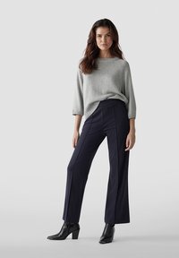 Grauer Strickpullover kombiniert mit weiten marineblauen Hosen und schwarzen Absatzstiefeletten. Das Outfit zeichnet sich durch einen lässigen Sitz mit strukturiertem Finish aus.