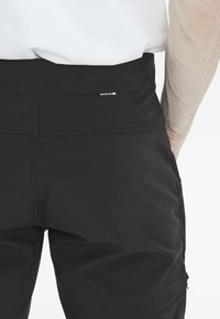 Svarta träningbyxor tillverkade av elastiskt material, med en slät textur och en liten "Whistler"-logotyp på baksidan av midjebandet.