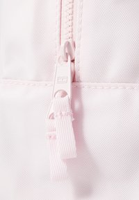 Ljusrosa syntetisk tyg med en texturerad yta, som har en matchande dragkedja och dragkedjeflik.