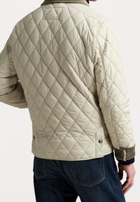 Beige quilted jacket featuring a diamond pattern, corduroy cuffs, and a stand collar, complemented by snap button accents.