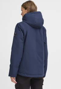 Veste à capuche bleu marine en matériau durable, avec une coupe décontractée, des coutures surpiquées et un détail de logo sur la manche gauche.