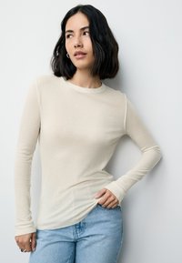 Top cu mâneci lungi, din bumbac bej deschis cu model striat, cu decolteu rotund și croială mulată, asortat cu blugi din denim albastru.