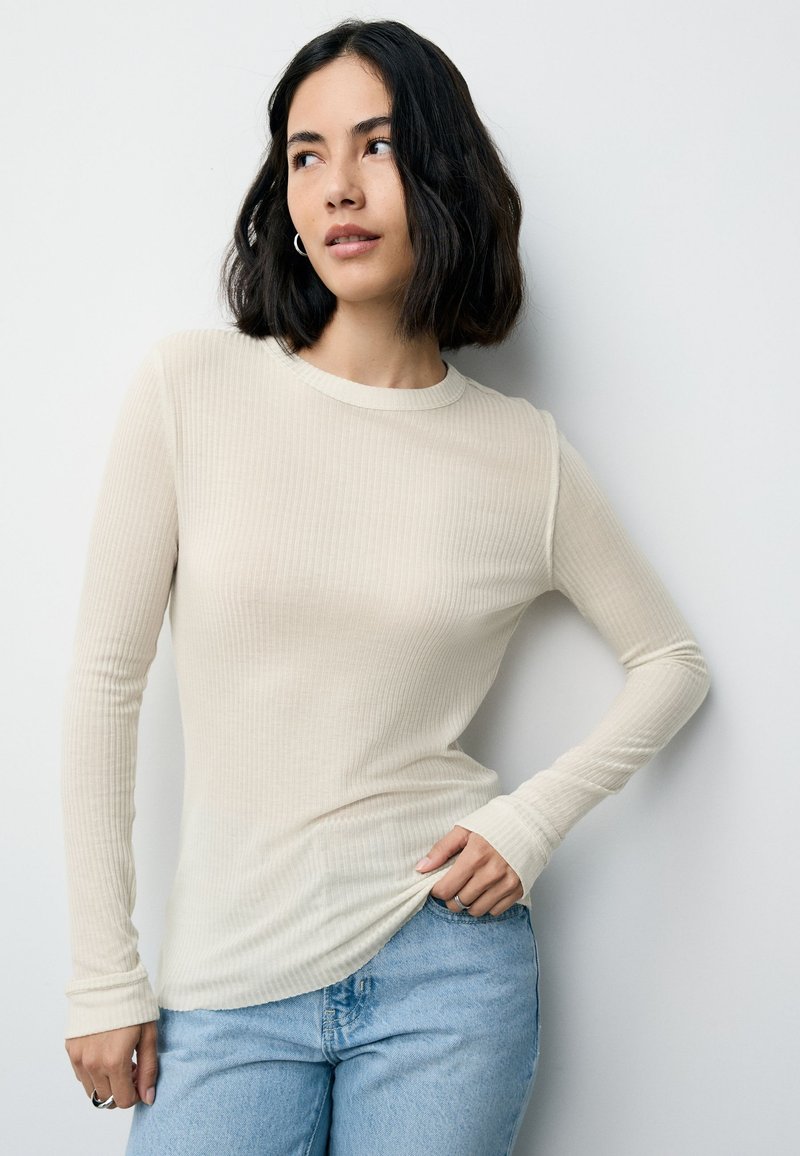 Top cu mâneci lungi, din bumbac bej deschis cu model striat, cu decolteu rotund și croială mulată, asortat cu blugi din denim albastru.