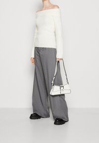 Maglione bianco soffice a spalle scoperte con maniche lunghe, abbinato a pantaloni grigi a gamba larga e una piccola borsa bianca con dettagli neri.