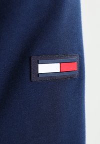 Tessuto di colore blu navy con una toppa marchiata che presenta strisce orizzontali blu, bianche e rosse, cucita sul lato sinistro.