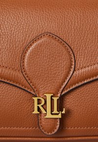 Brown leather handbag with a textured surface, gold "RLL" logo, and curved flap design featuring contrasting stitching details.