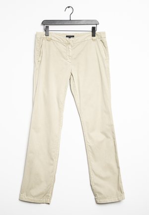 Chinos de algodón beige colgados en una percha negra; cuentan con bolsillos laterales, cierre de cremallera y diseño de pierna recta con costuras discretas.