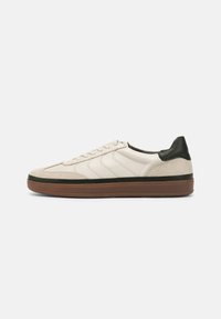 Lave topper sneakers i beige lær med suede accenter, med en mørkegrønn hæl og brun gummisåle. Diskret side stripe mønster.