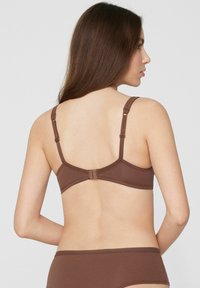 Hnědá bezdrátová podprsenka s nastavitelnými ramínky a zapínáním na háček, s hladkou texturou a jednoduchým designem.