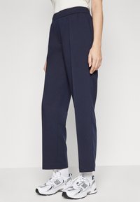 Pantalones de corte alto color azul marino, con una tela suave y texturizada, que presentan un diseño de pierna ancha y una cintura elástica. Combinados con zapatillas blancas.