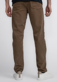Bruine corduroy broek met een verticale ribbeltextuur, twee achterzakken en een relaxed fit, gecombineerd met witte sneakers.