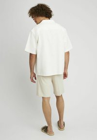 Chemise blanche à manches courtes avec une texture, associée à un short beige clair. Conçue avec une coupe décontractée et un style casual.