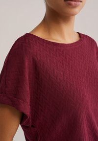 Bordo majica s kratkimi rokavi s teksturiranim vzorcem ribje kosti, okrogel izrez in zavihani rokavi, izdelana iz lahkega blaga.