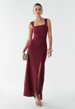 Vīna sarkanā maxi kleita ar kvadrātveida dekoltē, ribota tekstūra, šaurs griezums un sānu šķiršanās. Apvienota ar mazu soma un nūjām nūdu krāsā.