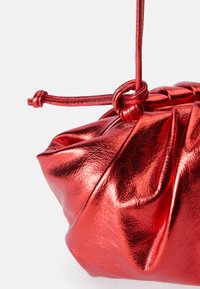 Red metallic clutch bag with a gathered design, featuring a knotted handle and a smooth, reflective texture. Compact shape with soft folds.