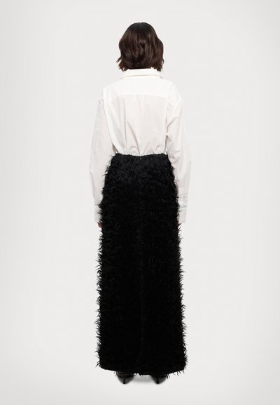 Jupe noire longue, avec un design texturé semblable à des plumes, assortie à une chemise blanche à col, vue de dos.