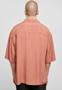 Camicia a maniche corte di colore rosa chiaro realizzata in tessuto morbido, caratterizzata da una vestibilità rilassata, colletto aperto e dettagli di cuciture pulite sul retro.