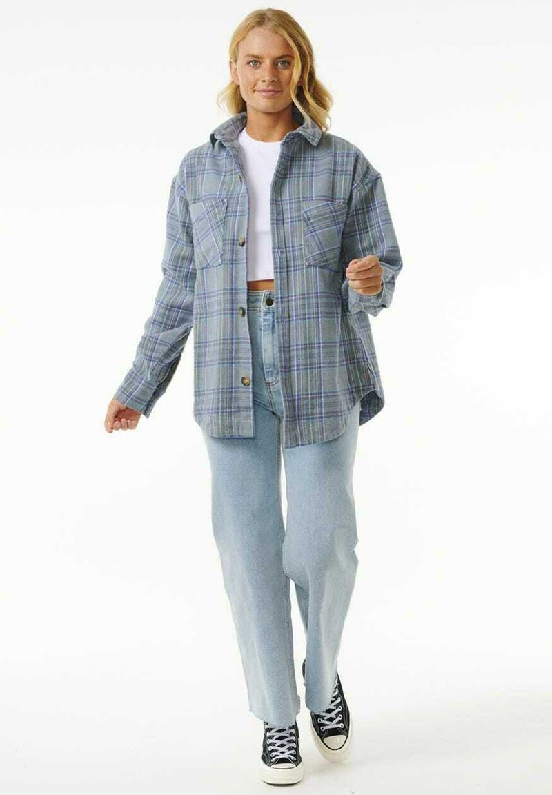 Camisa de cuadros en azul y verde, diseño de botones, con dos bolsillos frontales, combinada con jeans azul claro y zapatillas negras. Textura suave.