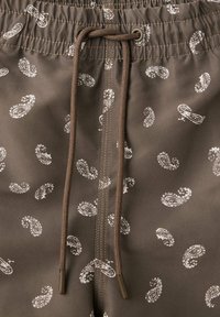 Tissu marron avec motif paisley blanc, comportant un cordon marron central et une ceinture élastique froncée sur un vêtement.