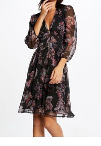 Sort kjole med gennemsigtige lange ærmer, en dyb V-hals og et figursyet skørt. Har et blomstret paisley-mønster i livlige farver.