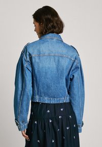 Lühi denim jakk helesinises toonis. Omab klassikalist kraed, nööbideta mansette ja õlavarre epauletti. Kerejoonega disain ning lühike pikkus.