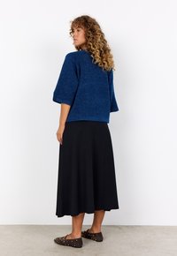 Blue knit top with short, wide sleeves, paired with a long black skirt. Soft texture, relaxed fit, and dark brown shoes with gold accents.