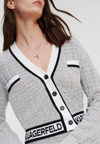 Szary kardigan o fakturze z czarno-białymi akcentami, z głębokim dekoltem w serek, guzikami z przodu i paskiem na talii z logo.