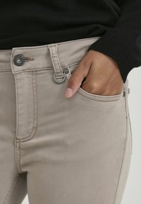 Pantalones de mezcla de algodón beige con cremallera y cierre de botón, con un bolsillo frontal y costuras decorativas a lo largo de las costuras.