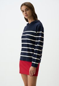 Maglione a righe navali con cappuccio e strisce bianche orizzontali, con polsini a costine, abbinato a una gonna rossa, che presenta un design casual.