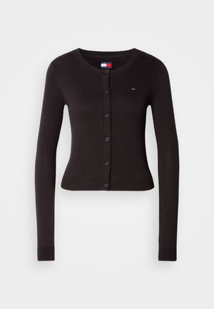 Crna dugačka kardigan sa dugim rukavima i okruglim izrezom, prednjim dugmadi, rebrastim manžetama i rubom. Ima mali logo na lijevoj strani grudi.