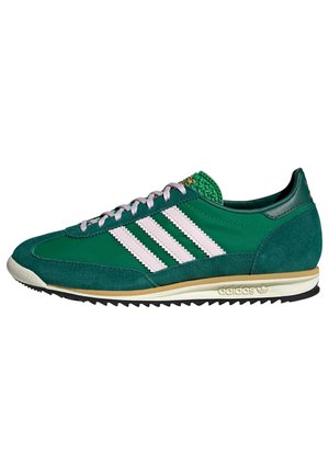 Groene Adidas-sneaker met witte strepen, suède en stoffen materialen, beige en zwarte zool, en witte veters, gezien vanaf de buitenkant.