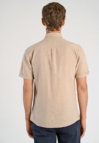 Camicia a maniche corte in tessuto beige chiaro con una texture sottile, colletto casual e dettagli con piega sul retro. Finitura liscia e vestibilità rilassata.