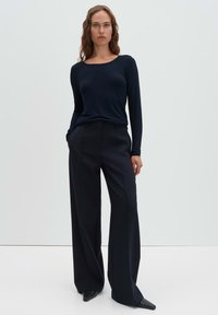 Langärmliges, marineblaues Strickoberteil mit Rundhalsausschnitt, kombiniert mit weiten, hochgeschnittenen schwarzen Hosen; elegante Textur und maßgeschneiderter Schnitt.