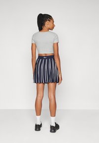 T-shirt gris court avec une jupe plissée bleu marine dotée de rayures verticales blanches. La taille est ornée de la marque "Guess." Des chaussures noires et des chaussettes blanches sont portées.