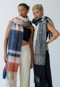 Deux mannequins portent de longues écharpes. Une écharpe présente un motif à carreaux bleu, rose et orange ; l'autre est noire avec des accents gris. Les deux ont une texture.