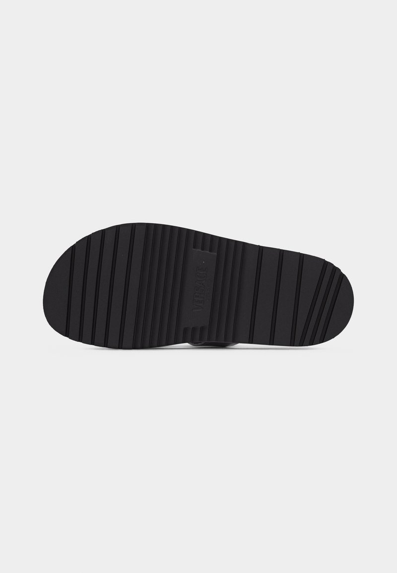 Black rubber shoe sole with horizontal grooves and Versace logo embossed at the center.