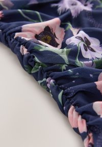 Tamsiai mėlynos spalvos susirinkusi medžiaga su rožinėmis, baltomis ir levandinėmis gėlėmis bei žaliomis lapeliais arti.