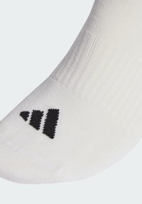 Calcetín blanco con textura acanalada, que presenta un logo negro de tres franjas en la punta. El material parece suave y elástico.