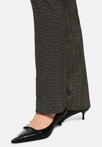 Schwarze spitz zulaufende Kitten-Heels, getragen mit braunen und schwarzen gemusterten geraden Hosen.