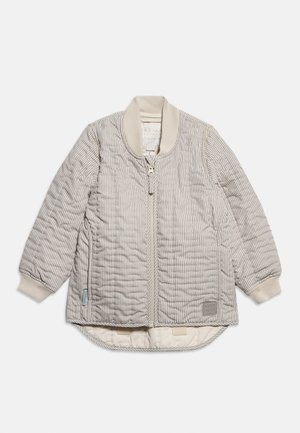 Jasno beżowa pikowana kurtka z pionowymi paskami, prążkowanym kołnierzem i mankietami, przednim zamkiem błyskawicznym oraz wyprofilowanym dołem, który z tyłu jest dłuższy.