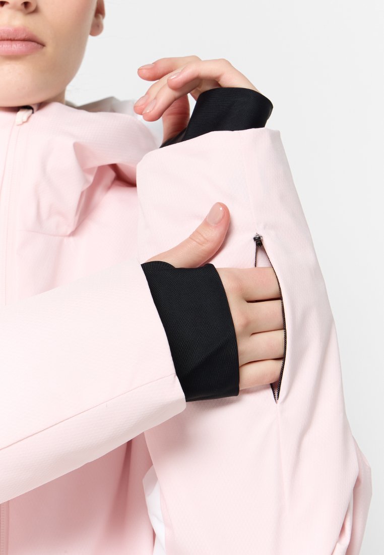 Giacca rosa chiaro con una superficie testurizzata, caratterizzata da polsini neri a contrasto e una tasca con zip sulla manica. Focus sui dettagli del tessuto e delle funzionalità.