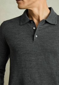 Polo din material moale, texturat, de culoare gri închis, cu mâneci lungi; are un guler și trei butoane albe la guler.