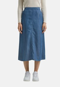 Jeanskjol i midilängd i ljusblått med en centrerad söm, elastisk midjeband och subtil fåll, kombinerad med vita sneakers.