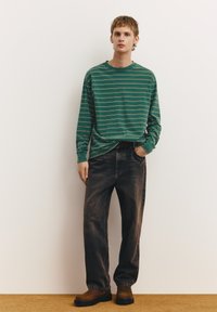 Cămașă verde cu mâneci lungi, cu dungi albe subțiri, asortată cu blugi largi din denim închis și cizme maro până la gleznă. Design simplu și croială lejeră.