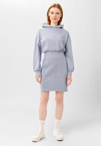 Felpa azzurra chiara con una vestibilità comoda e maniche lunghe, abbinata a una gonna aderente coordinata. Il modello indossa sneaker bianche e calzini al polpaccio.