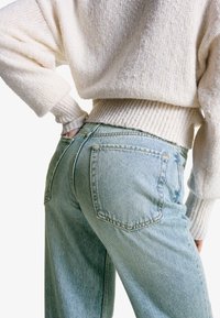 Lysblå højtaljede jeans med en afslappet pasform, der har dekorative baglommer, sammen med en cremegul, tekstureret striktrøje.