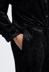 Conjunto de loungewear de terciopelo negro que incluye una camisa abotonada con puños y pantalones a juego, ambos con una superficie suave y texturizada.