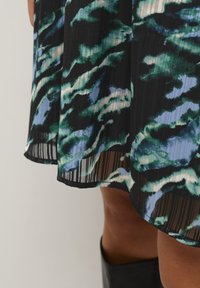 Robe noire avec une texture plissée arborant un motif abstrait vert et bleu, finition avec un ourlet courbé et un design superposé.